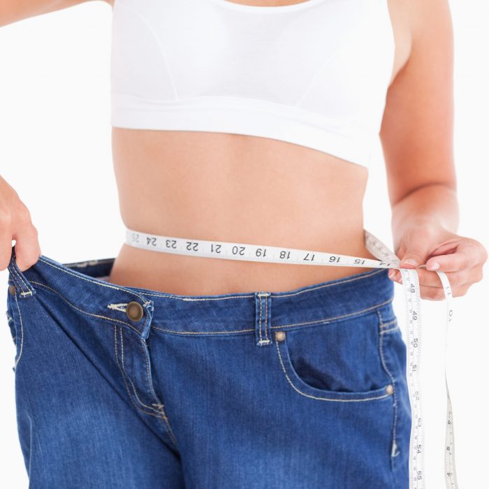Woman measuring her waist while wearin too big jeans in a studio